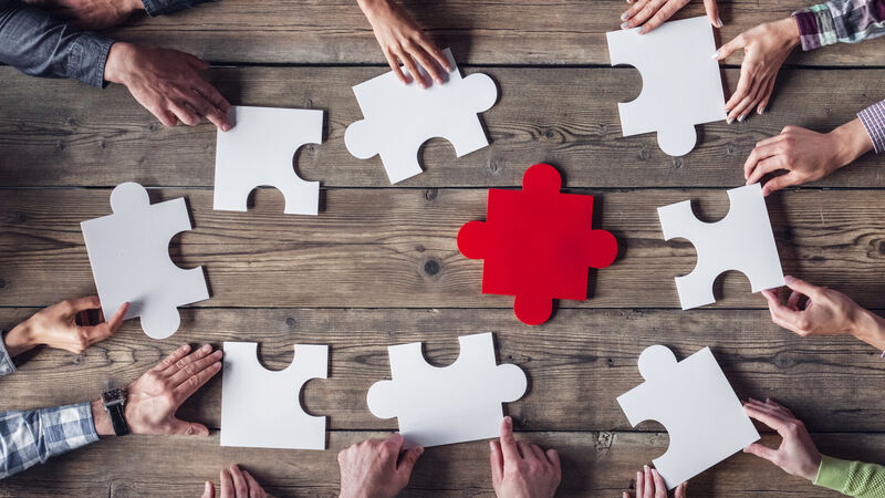 Graphic showing human hands around a table putting large puzzle pieces together.