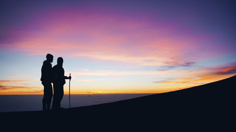 Two people beginning a hike up a hill at sunrise.