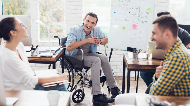 A small group of young adults is having a big laugh during a study group, the member pictured center is a wheelchair user.