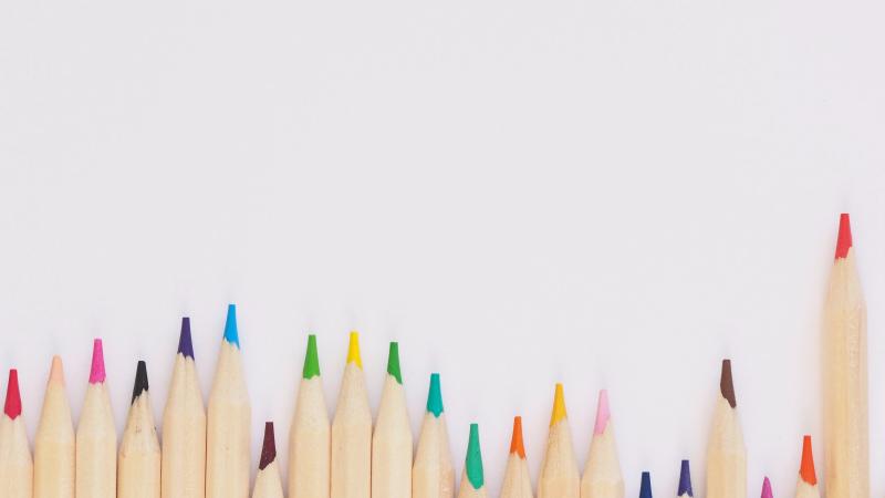 A series of freshly sharpened multi-colored pencils lined up together on a light background.