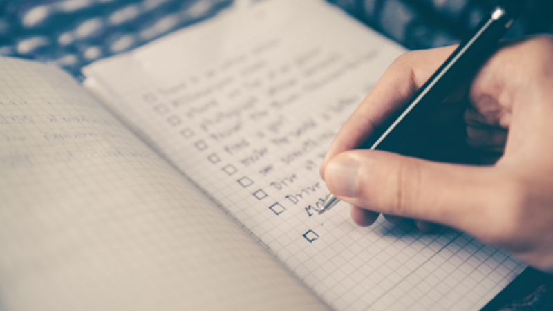 Person with a pen writing a list of items in a notebook.
