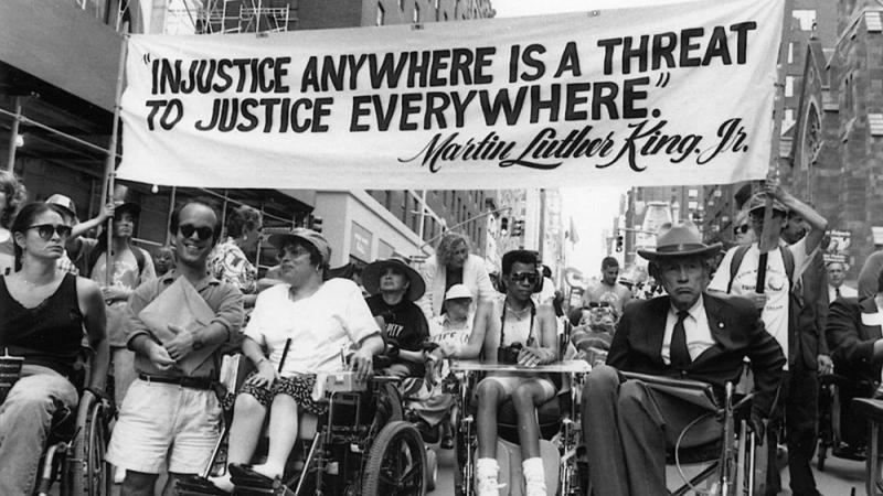 Disabled protesters underneath a banner that reads "Injustice anywhere is a threat to justice everywhere."