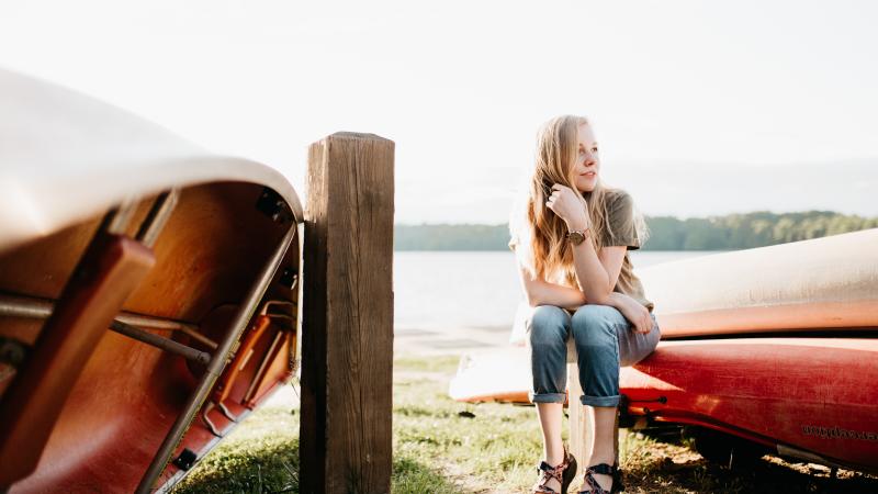 Woman sitting near canoes by lake