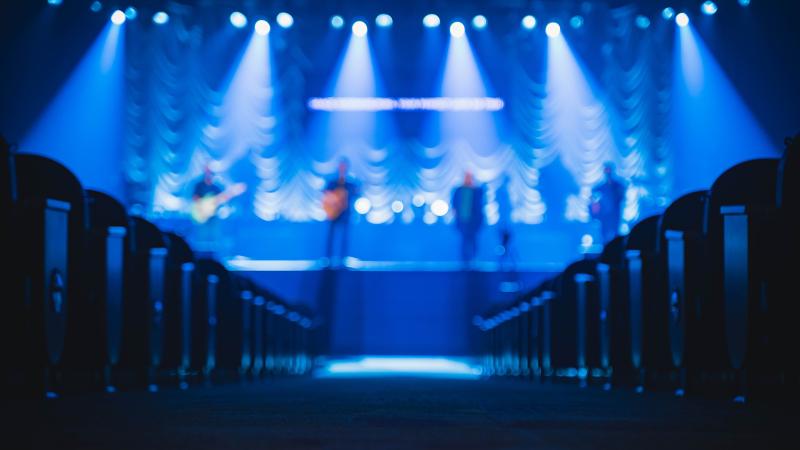 People on a stage playing instruments, empty seats.