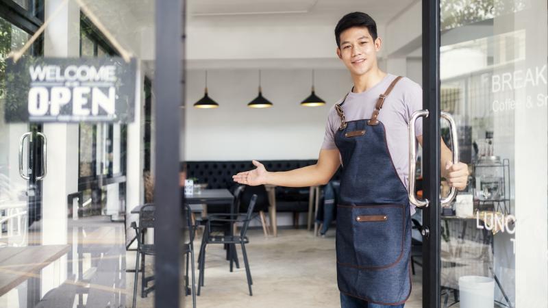 Man holding a door open to welcome in customers.