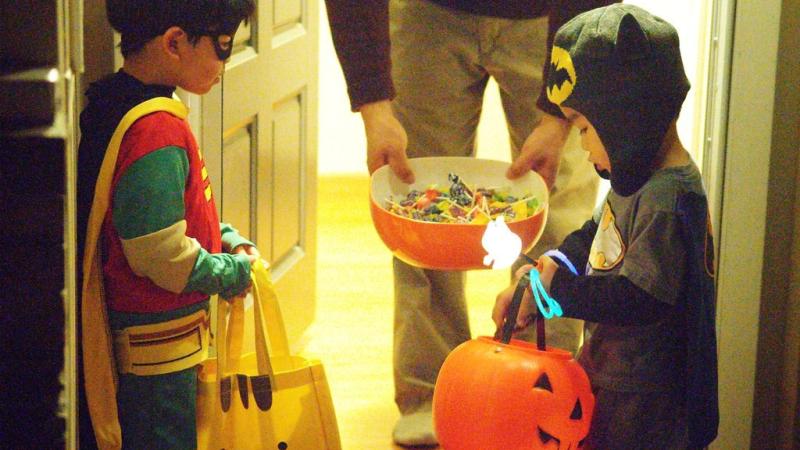 Two children dressed in Halloween costumes are receiving Halloween candy at someone's front door.