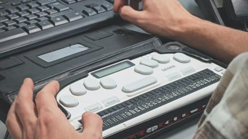 A picture of a person using a refreshable Braille display with a computer.