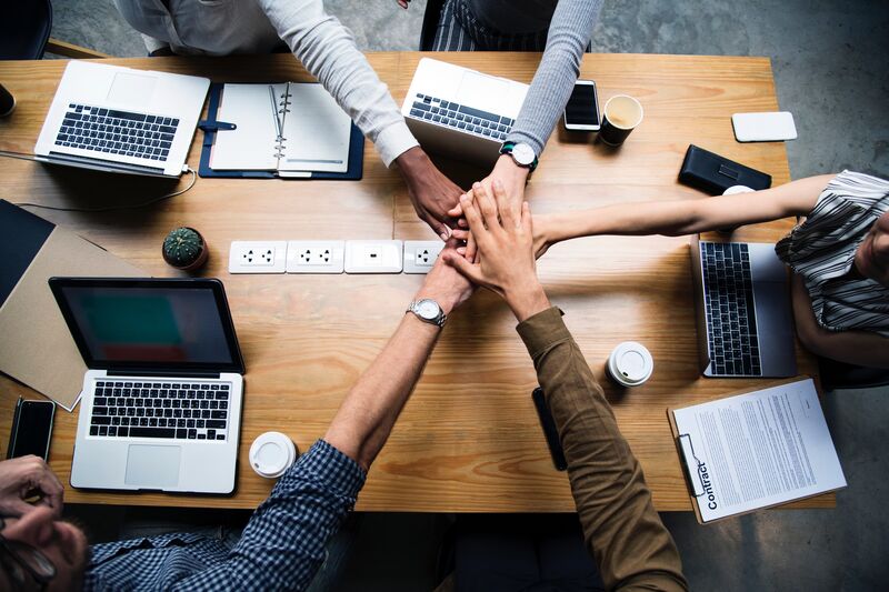 Five hands meeting in the middle of a table in partnership.