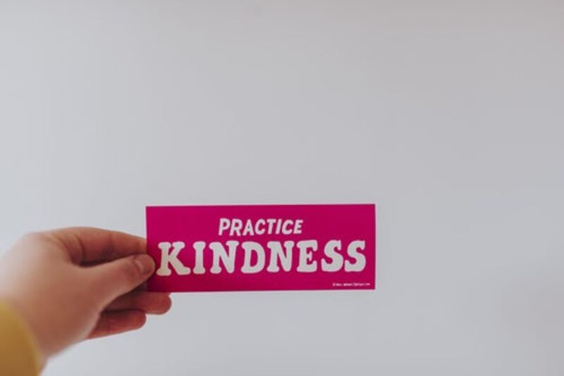 person holding red and white practice kindness sticker