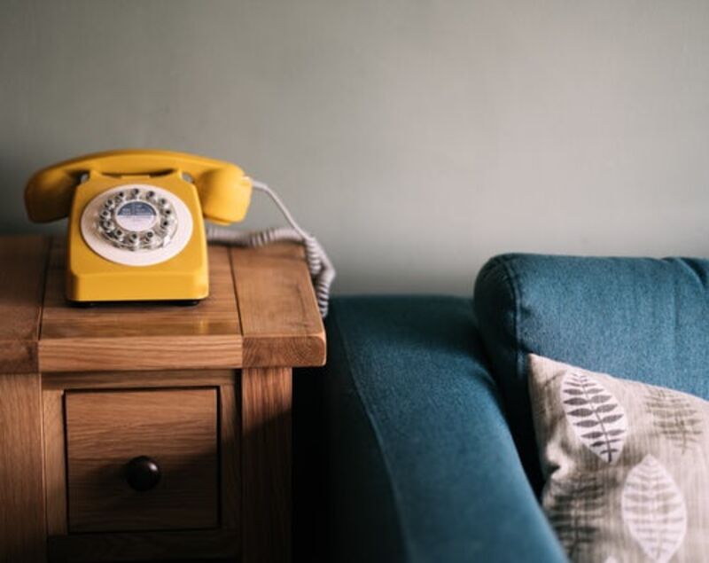 A yellow rotary phone on a table next to a blue sofa.