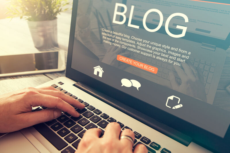 A person accessing a blog website on their laptop sitting on a desk with the sun shinning in in the background.