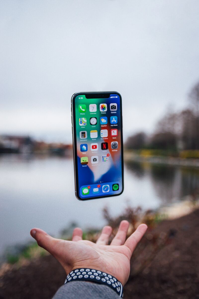 A person holding out their hand with their palm up and an iPhone floating above their hand, open and showing all the apps.