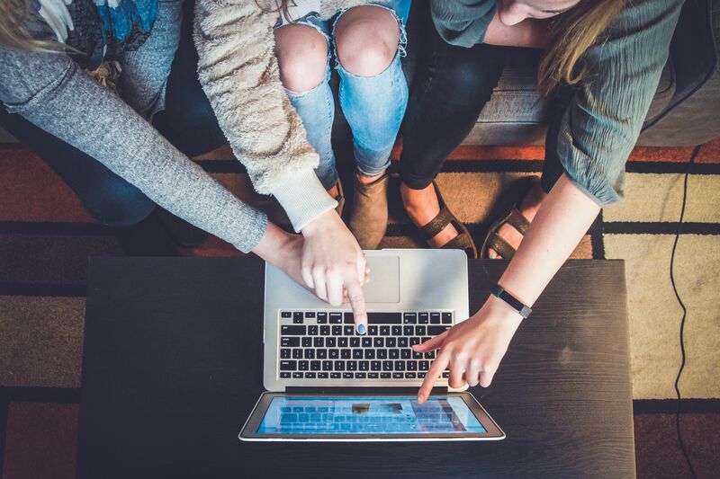 A group of three people sitting in front of a laptop sitting on a coffee table, accessing an online learning module.