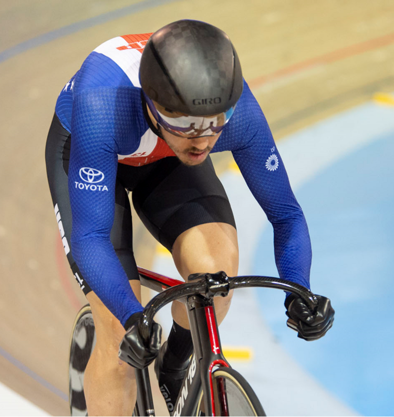 Photo of Chris Murphy wearing a Team USA speedsuit slowly winding up speed at the top of a velodrome racing track.