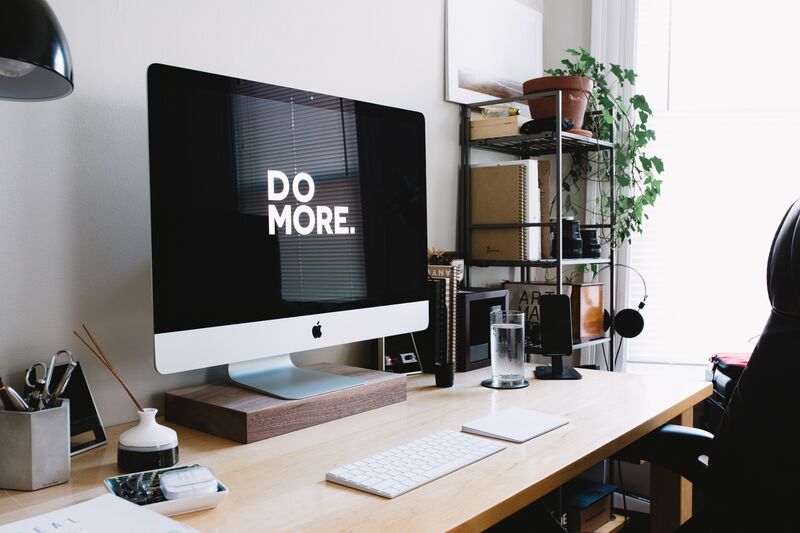 A large desktop monitor sitting on a desk with the words do more typed on screen in a home office.