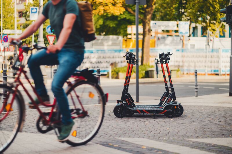 E-scooters are parked on a sidewalk as someone on a bike rides past.