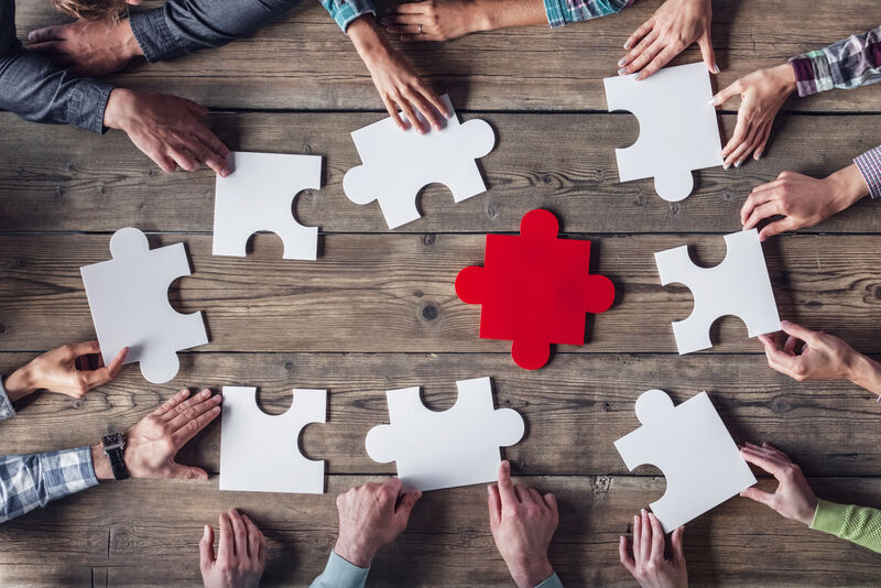 Graphic showing human hands around a table putting large puzzle pieces together. 