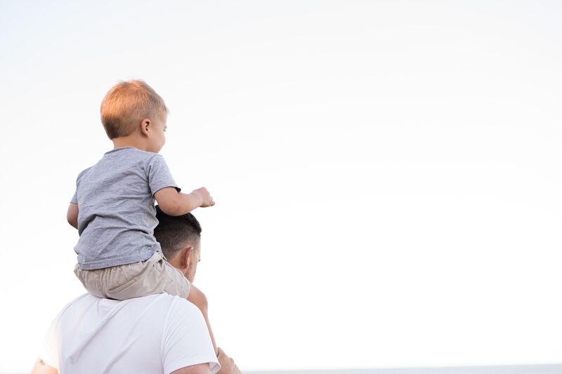 A man with a small child on his shoulders looking away from the camera.
