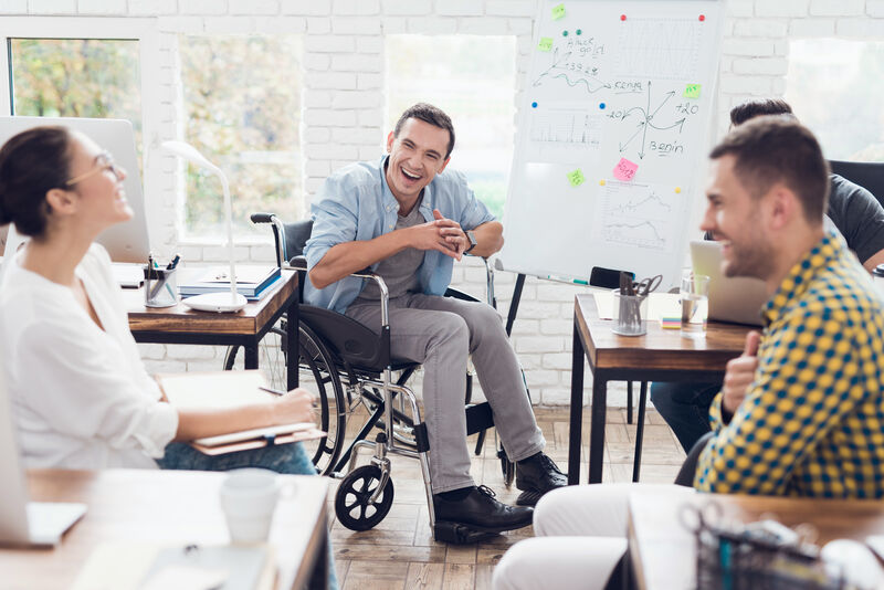 A small group of young adults is having a big laugh during a study group, the member pictured center is a wheelchair user.