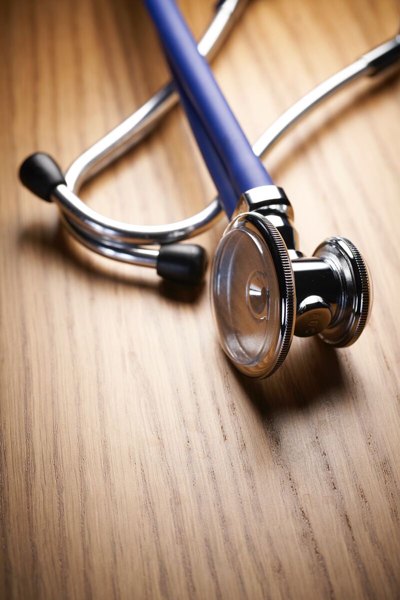 A doctor’s stethoscope is laying on a wooden table, with the chest piece laying over the earpieces.