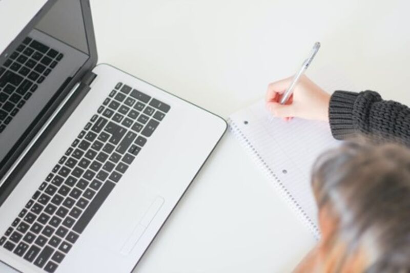 Overhead, close-up shot of woman at computer, taking notes with a pen