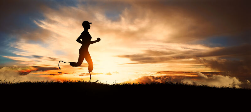 A lone runner with bladed lower legs shown in profile as a dark figure against a setting sun in a cloudy sky in the background.