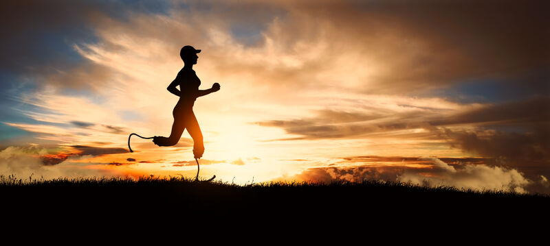 A lone runner with bladed lower legs shown in profile as a dark figure against a setting sun in a cloudy sky in the background. 