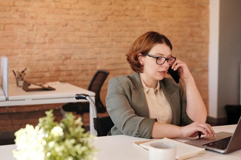 A woman answers the phone while working at her laptop.