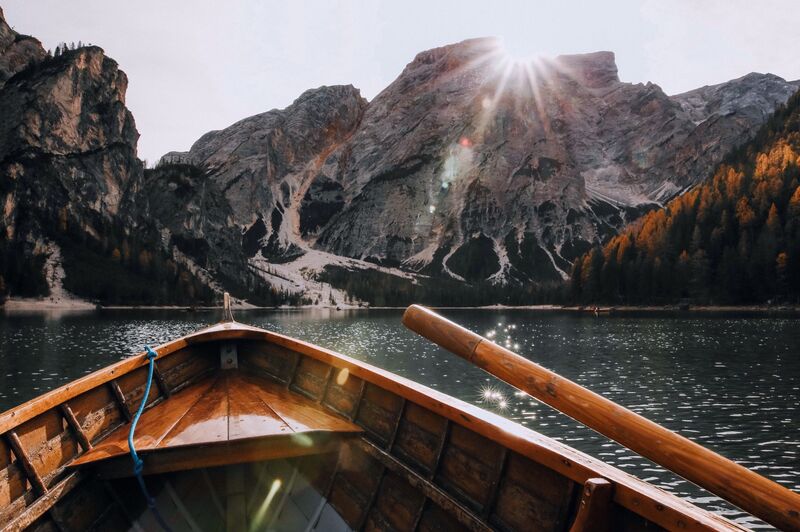 The bows of a small boat approaching mountains on the shoreline, surrounded by calm waters.