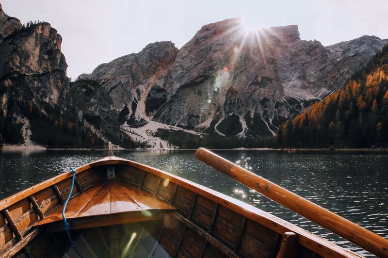 The bows of a small boat approaching mountains on the shoreline, surrounded by calm waters.   