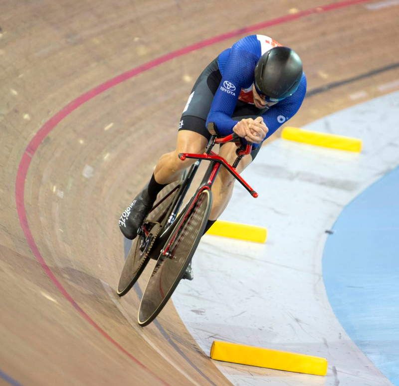 The blog author racing his track bike on a banked wooden track, hunched over in an aerodynamic position. 