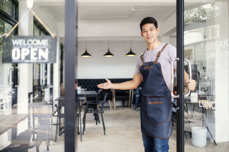 Man holding a door open to welcome in customers. 