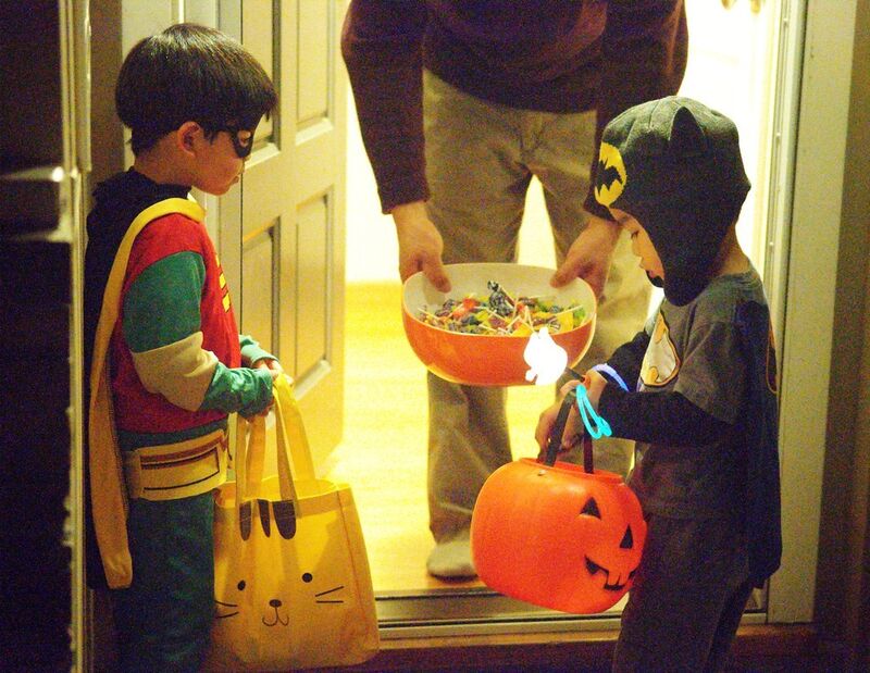 Two children dressed in Halloween costumes are receiving Halloween candy at someone's front door.