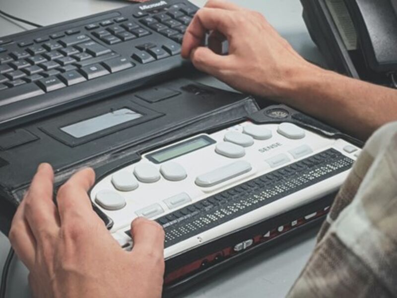 A picture of a person using a refreshable Braille display with a computer. 