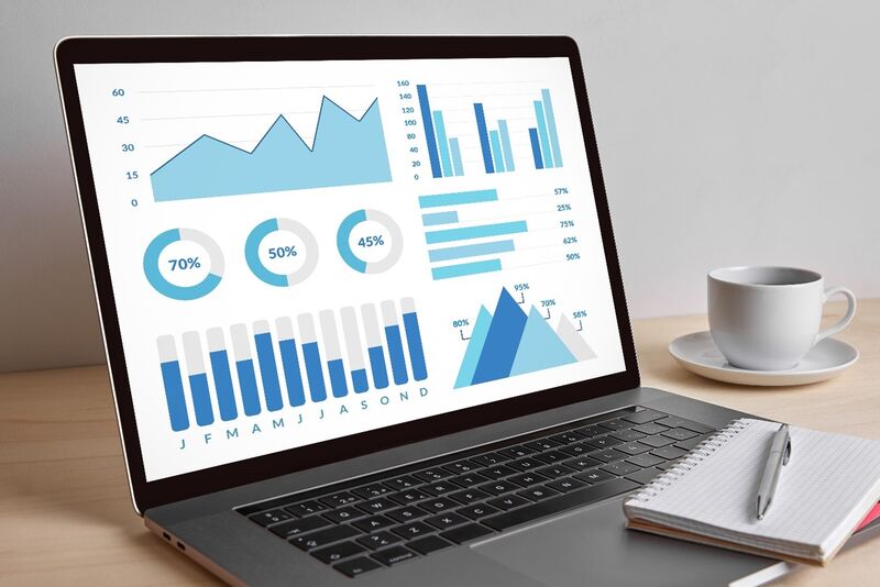 A desk with a cup of coffee, a notepad, and computer displaying an infographic. 