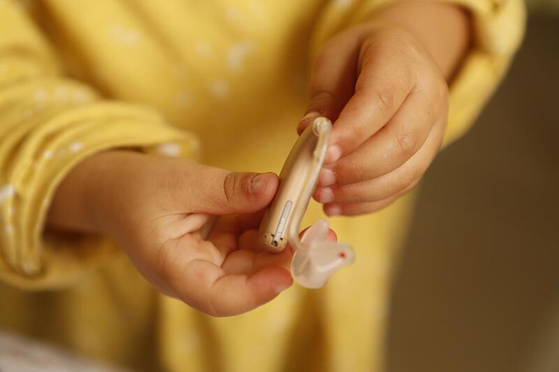 a child wearing a yellow sweater, holding a hearing aid