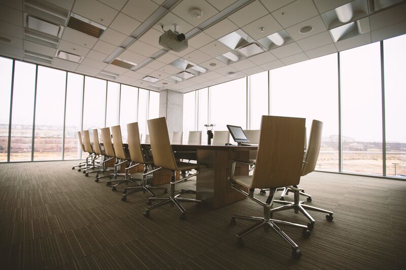a long conference room table surrounded by empty chairs in a room with many windows