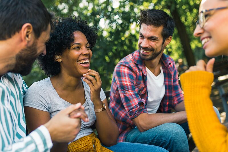 a black, curly haired woman wearing a hearing aid while having a delightful conversation with friends at a park