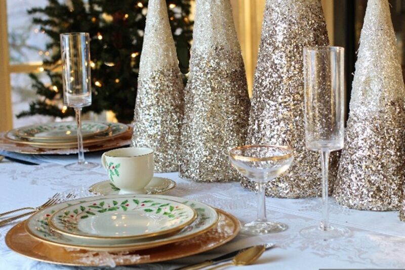 a place setting for a holiday dinner including plates, silverware, and glasses placed in front of gold, glittery, decorative table trees