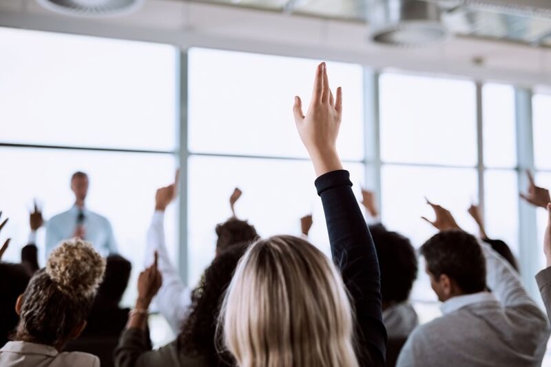a handful of people raising their hands, their backs to the camera