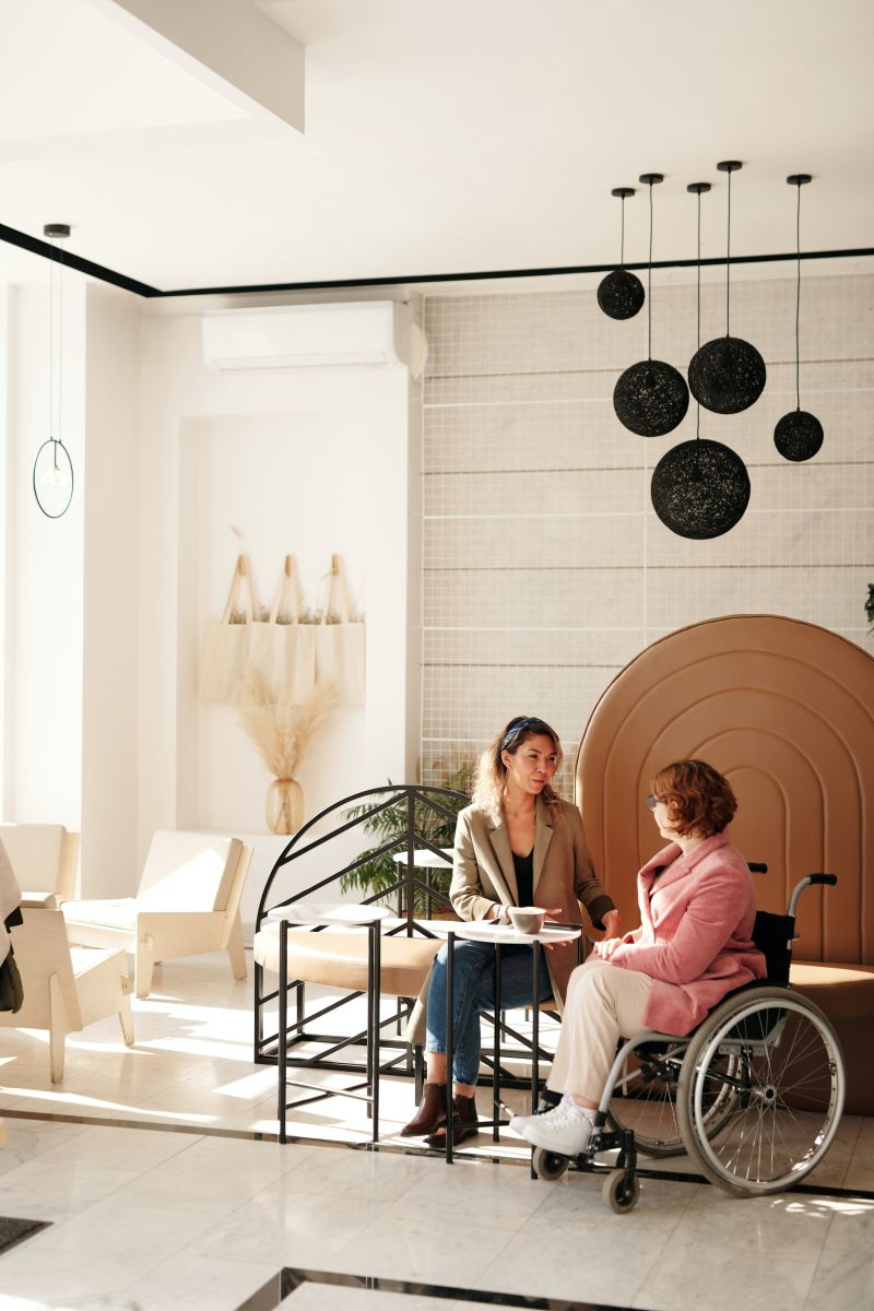 Two women meeting in hotel lobby dressed business casual, one in wheelchair