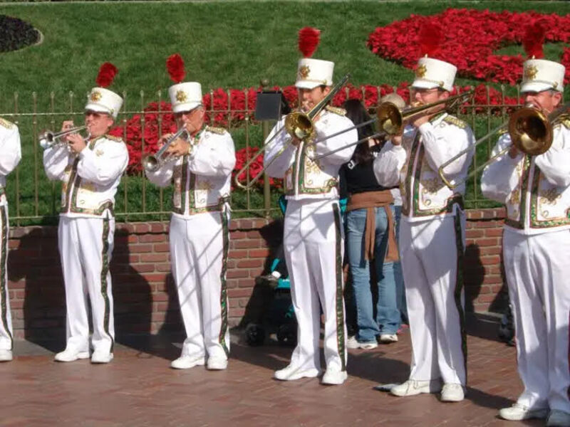 A photo of 5 brass players performing music in the Disneyland Band. The author of this post is center playing trombone in a white marching band uniform.