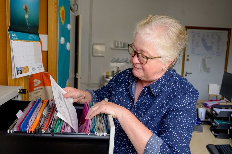 a white older adult woman looking at paper files in the office