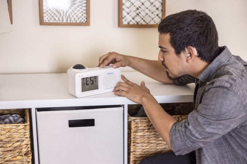 a young man with black hair wearing a hearing aid testing a vibrating alarm