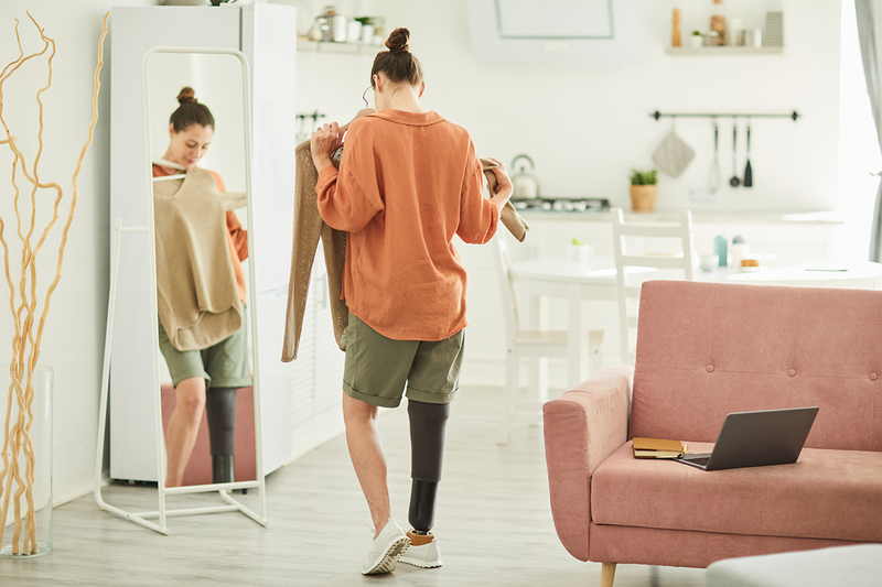 A person with a prosthetic limb looks in the mirror while trying on clothing. 