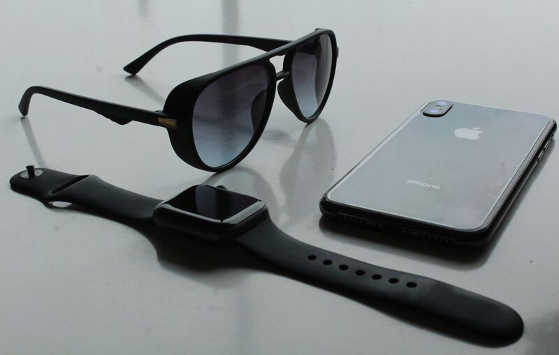 a black sunglasses, a black Apple watch and a black iPhone on a table