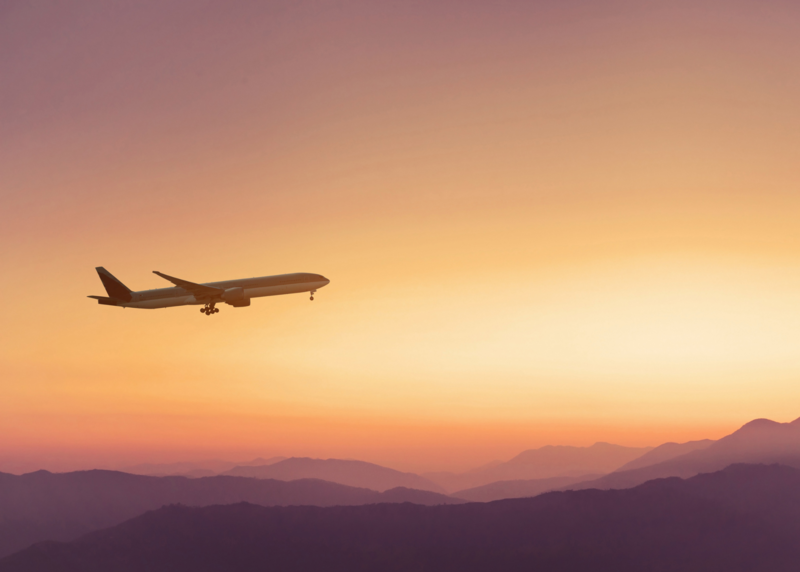 an airplane flying in the sky with purple mountains in the background at sunset