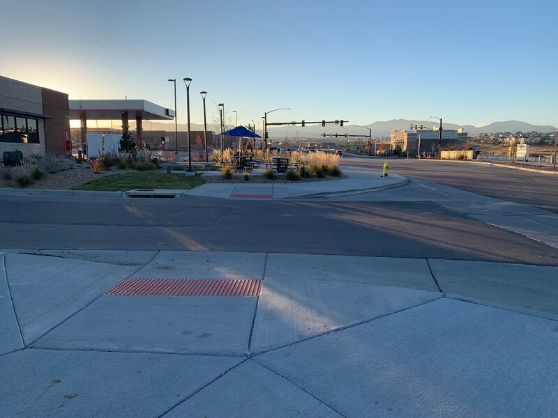 A recently completed project of an accessible curb ramp/crosswalk taken at sunset with commerce, residential neighborhoods, and mountains leading to the horizon.