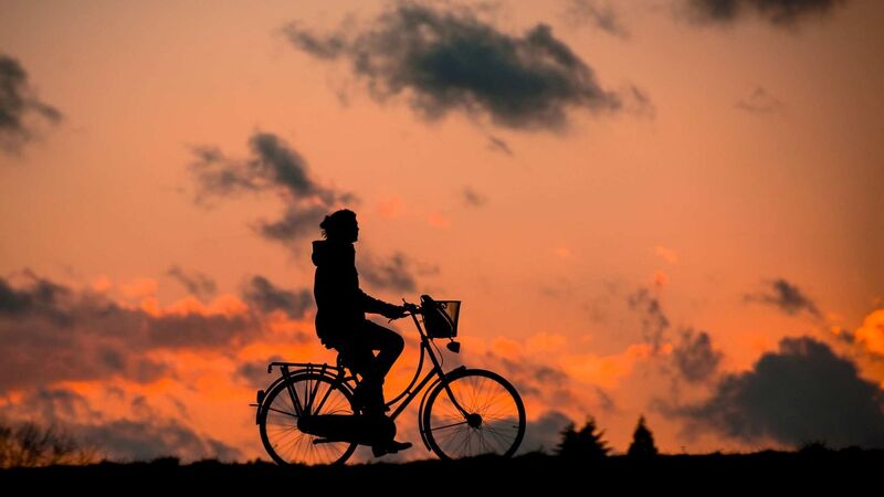 Silhouette of a person on a bike, with a sunset background. 