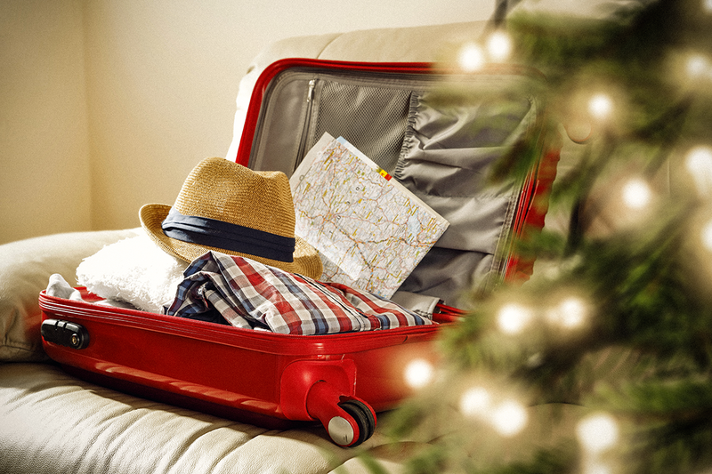A red suitcase filled with clothing and a brightly lit Christmas tree on the right.